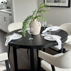 a dining room table with white chairs and a vase filled with greenery on it