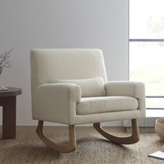 a white rocking chair sitting on top of a hard wood floor next to a window