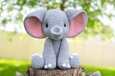 a crocheted elephant sitting on top of a tree stump