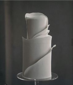 a three tiered cake with white icing on a glass stand in front of a dark background