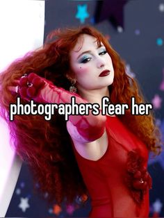 a woman with long red hair is holding her hand up to the camera and looking into the