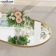 a vase filled with flowers sitting on top of a table next to a mirror that says hawkings