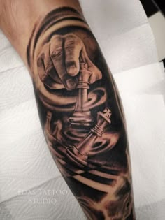 a man's arm with a black and grey tattoo on it, holding a chess piece