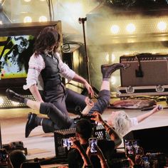 a man is jumping in the air on stage with his legs spread out as people take pictures