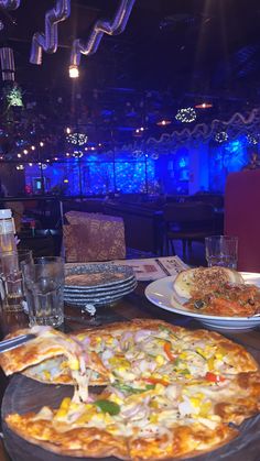 a large pizza sitting on top of a table next to plates of food and drinks