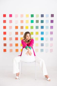 a woman sitting on top of a white chair in front of a wall with color swatches