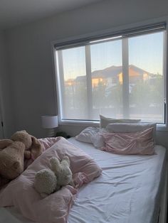 two teddy bears sitting on top of a bed in front of a window with blinds