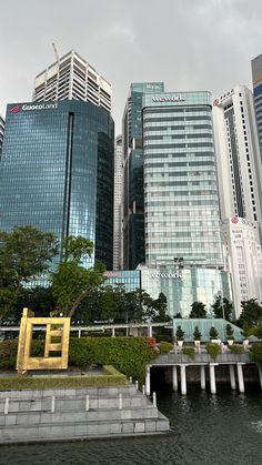 some very tall buildings by the water and stairs in front of them with a yellow sculpture