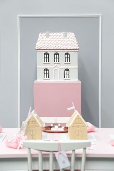 a pink and white cake sitting on top of a table next to two small houses