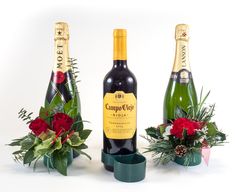 three bottles of champagne and flowers in vases on a white background with red roses