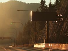 the sun is shining down on an empty highway with trees in the background and mountains in the distance