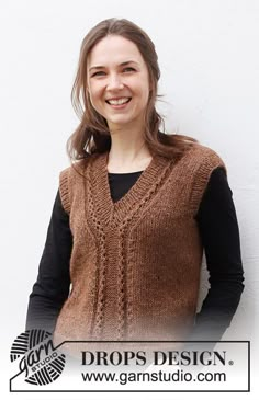 a woman standing in front of a white wall wearing a brown sweater and black shirt