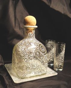 an ornate glass bottle and two glasses on a black tableclothed cloth with a wooden top