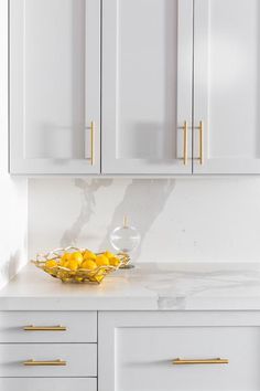 a bowl of lemons sitting on top of a kitchen counter next to white cabinets