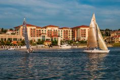 two sailboats sailing in the water near a large building with red roof and windows