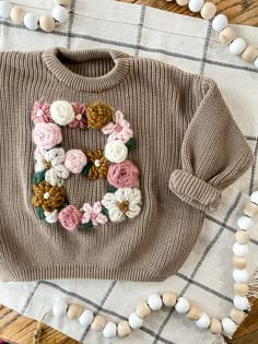 a sweater with flowers on it sitting on top of a table next to white and brown balls