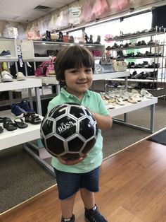 a young boy holding a soccer ball in a shoe store