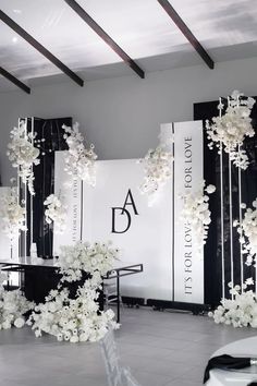 a room filled with white flowers and black tables in front of large wall hangings