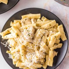 two black plates filled with pasta and meat covered in parmesan cheese on a marble table