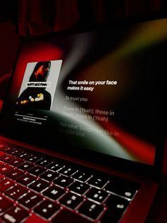 an open laptop computer sitting on top of a red table next to a black wall