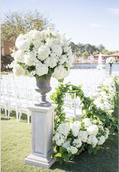 a tall vase filled with white flowers sitting on top of a lush green field next to chairs