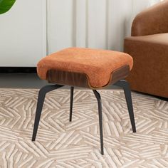 an orange ottoman sitting on top of a rug next to a brown chair and potted plant