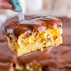 a person holding a piece of cake with chocolate frosting on it and a spatula