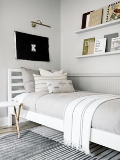 a white bed sitting in a bedroom next to a wall mounted book shelf with books on it