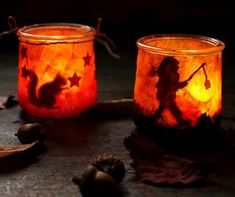 two glass jars filled with candles sitting on top of a wooden table next to leaves