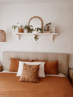 a bed with orange sheets and pillows in a white room next to some shelves filled with potted plants