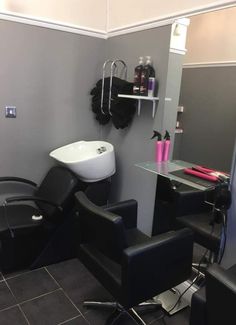 a hair salon with black chairs and a sink in the back ground, there is a mirror on the wall next to it