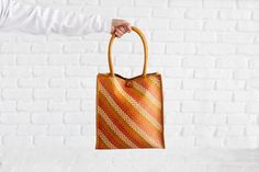 Handwoven Seagrass Tote, Orange Tote Bag With Handles, Straw Shopping BagOur totes are as functional as they are beautiful. Naturally dyed and lovingly handwoven, we know they will be a vibrant addition to your closet or as a gift. These totes are made by weavers in Chiangmai, Thailand where they use the Pandanus leaf as their material. 12"H x 11"W20"H x (with handle)The tote can hold up to 4lbs. Just enough to hold your MacBook.SOCIAL IMPACT | FAIR TRADE | HANDMADEYour purchase supports the bas Brown Square Beach Bag For Shopping, Brown Square Beach Shopping Bag, Orange Woven Bag For Shopping, Yellow Rectangular Straw Bag For Everyday, Orange Rectangular Beach Bag For Shopping, Everyday Yellow Rectangular Straw Bag, Orange Handheld Beach Bag, Orange Woven Straw Bag For Daily Use, Orange Woven Beach Bag For Shopping