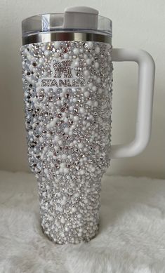 a white coffee cup with lots of silver beads on the bottom and handle is sitting on a fluffy surface