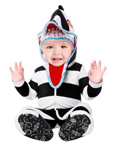 a baby wearing a penguin costume sitting on the ground with his hands in the air