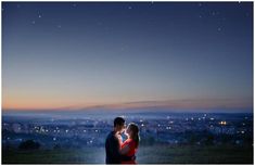 a man and woman standing next to each other on top of a hill