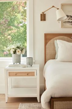 a white bed sitting next to a window with flowers on top of the headboard