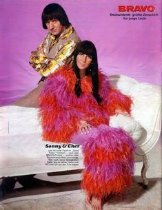 an old photo of two people sitting on a white couch with pink and orange feathers