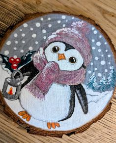 a painting of a penguin holding a christmas tree ornament on a wood slice