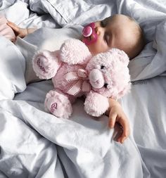 a baby laying in bed with a pink teddy bear and pacifier on its nose