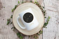 a white coffee cup sitting on top of a wooden table covered in green leaves and plants