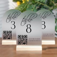 three clear acrylic signs with black numbers on them sitting on a wooden table