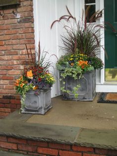 two cement planters with flowers in them sitting on the front step of a house