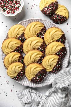 chocolate covered cookies with sprinkles on a white plate next to other dessert items