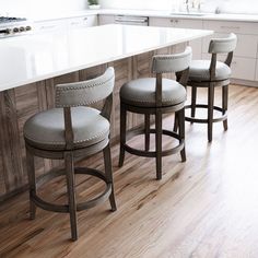 three stools sitting in front of a kitchen island with white counter tops and wood flooring