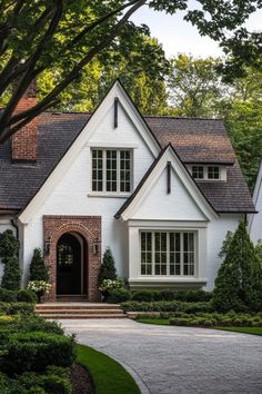 a white house with black trim and windows in the front yard is surrounded by greenery