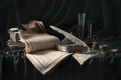 an old book and some other items on a black table cloth with a feather quill