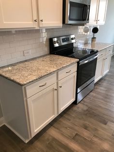 an empty kitchen with white cabinets and granite counter tops, black stove top oven and microwave