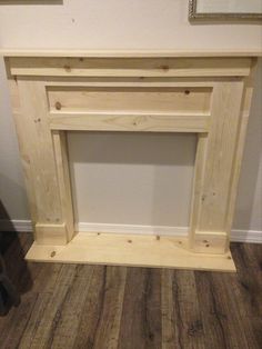 a wooden fireplace surround in a room with wood flooring and white paint on the walls