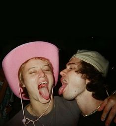 two young men with their mouths open wearing pink hats and headphones, one is sticking his tongue out to the other