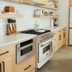 a kitchen with wooden cabinets and white counter tops, two ovens and open shelving